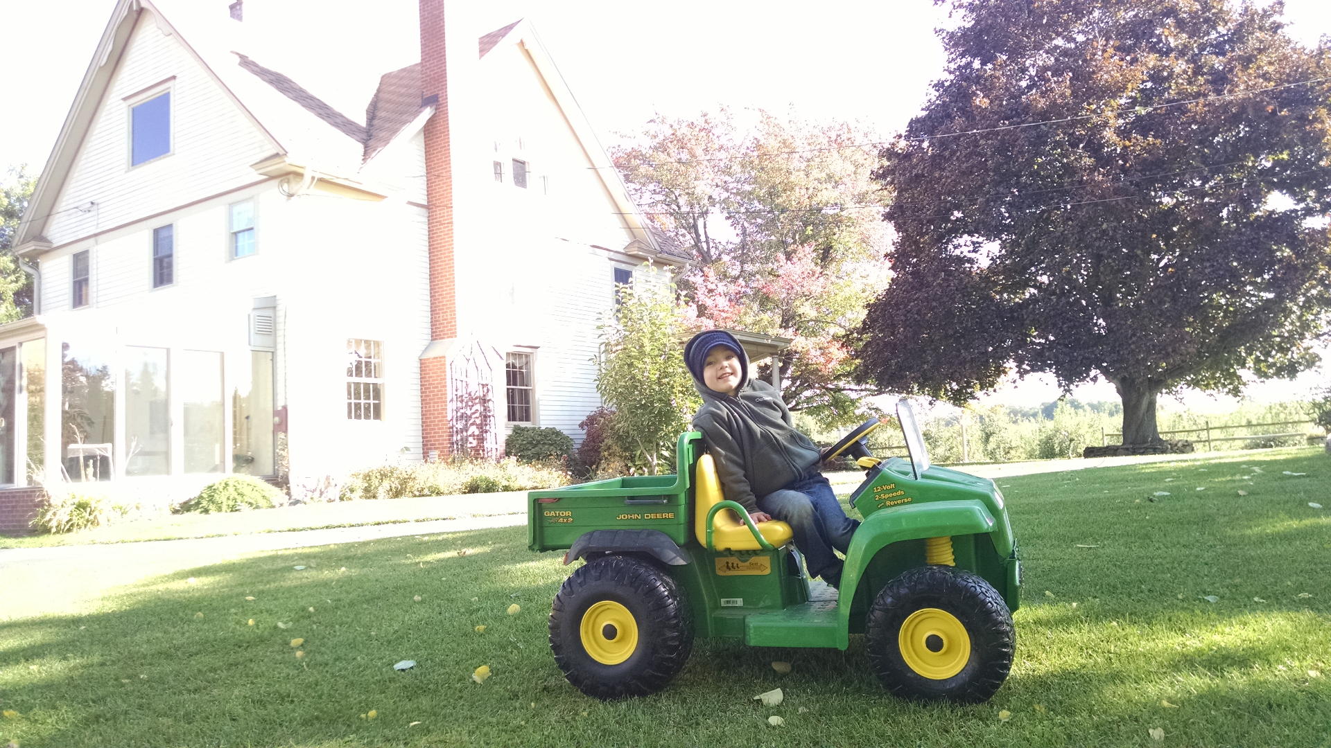 Casen sitting in a John Deere Gator ride-on toy in front of the farmhouse