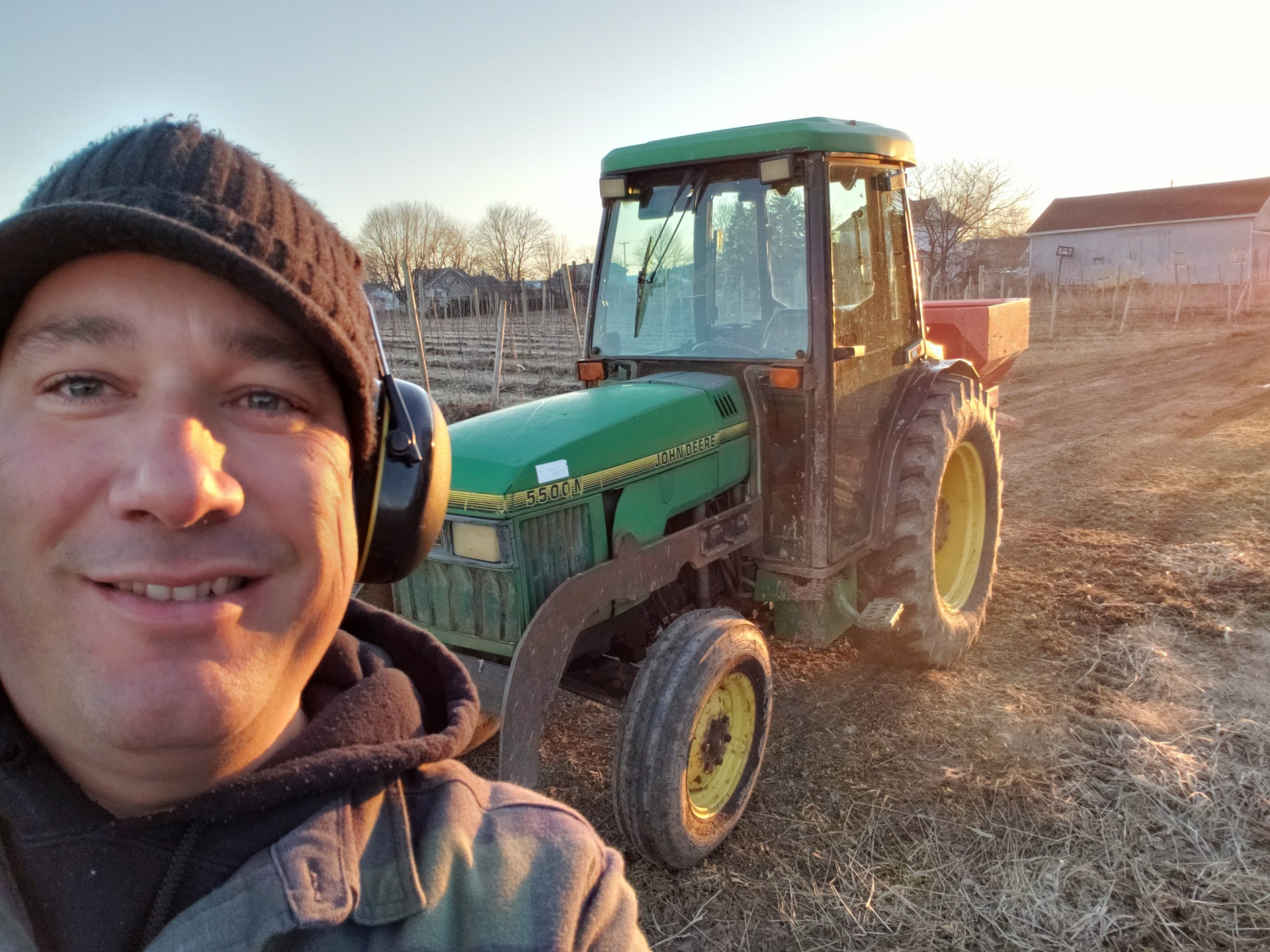 Jason on a John Deere tractor spreading fertilizer in a young orchard at sunrise